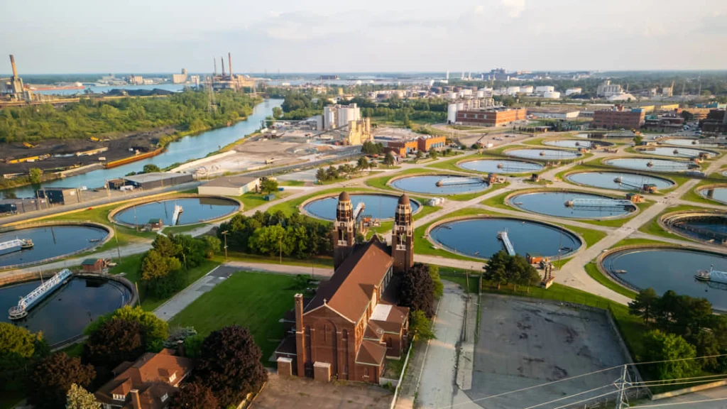 Luchtfoto van ronde waterbassins en een bakstenen gebouw met torens van een oud pompstation langs een rivier bij Detroit