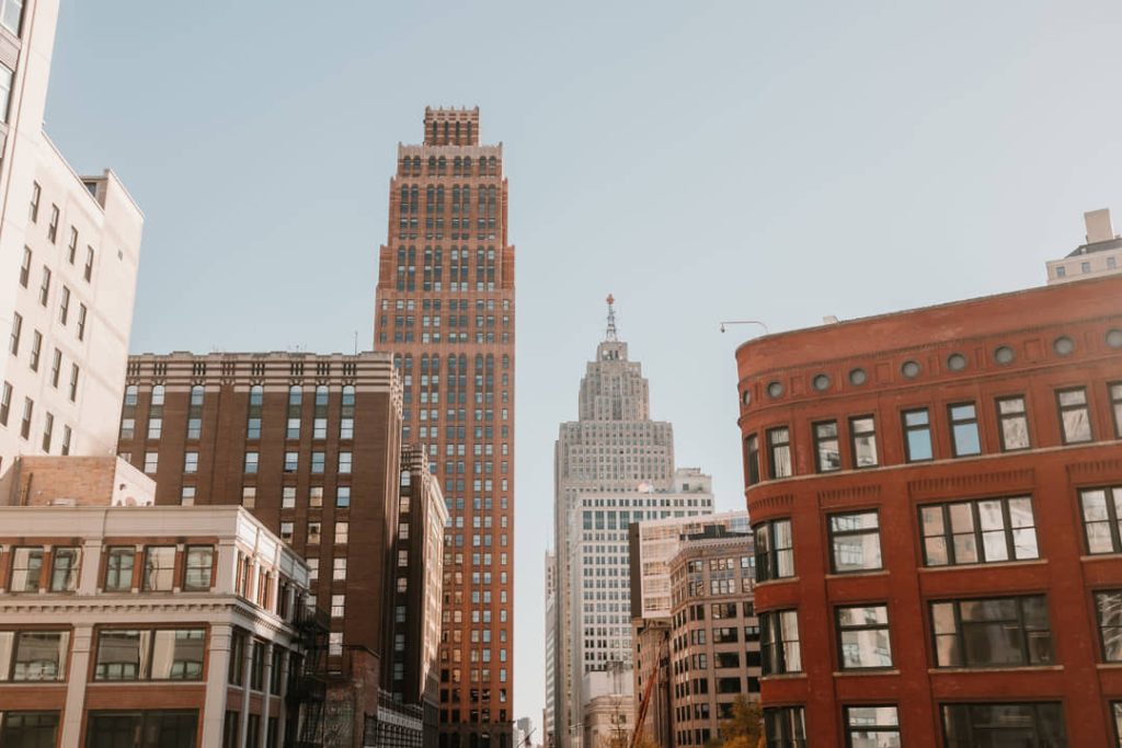 Straatbeeld met een hoge bakstenen wolkenkrabber met puntdak en omliggende gebouwen in het centrum van Detroit