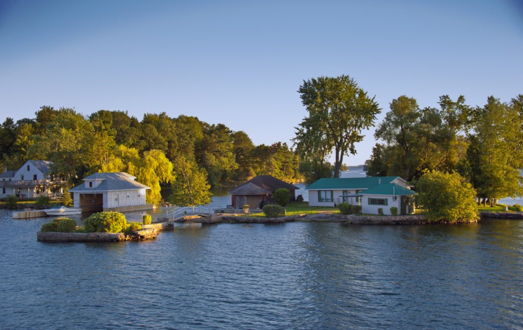 Verspreide vakantiehuizen met bootschuurtjes staan tussen bomen op een klein rotsachtig eilandje in de rivier bij avondlicht