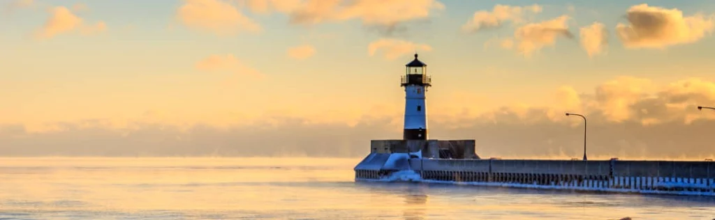 Witte vuurtoren aan het einde van een pier in Duluth, met opstijgende mist boven het water bij zonsopgang
