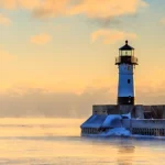 Witte vuurtoren aan het einde van een pier in Duluth, met opstijgende mist boven het water bij zonsopgang