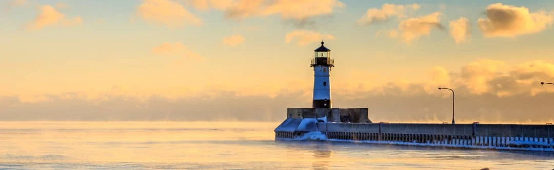 Witte vuurtoren aan het einde van een pier in Duluth, met opstijgende mist boven het water bij zonsopgang