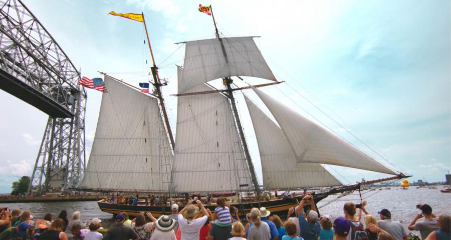 Historisch zeilschip met witte zeilen vaart voorbij de Aerial Lift Bridge tijdens Festival of Sail in Duluth