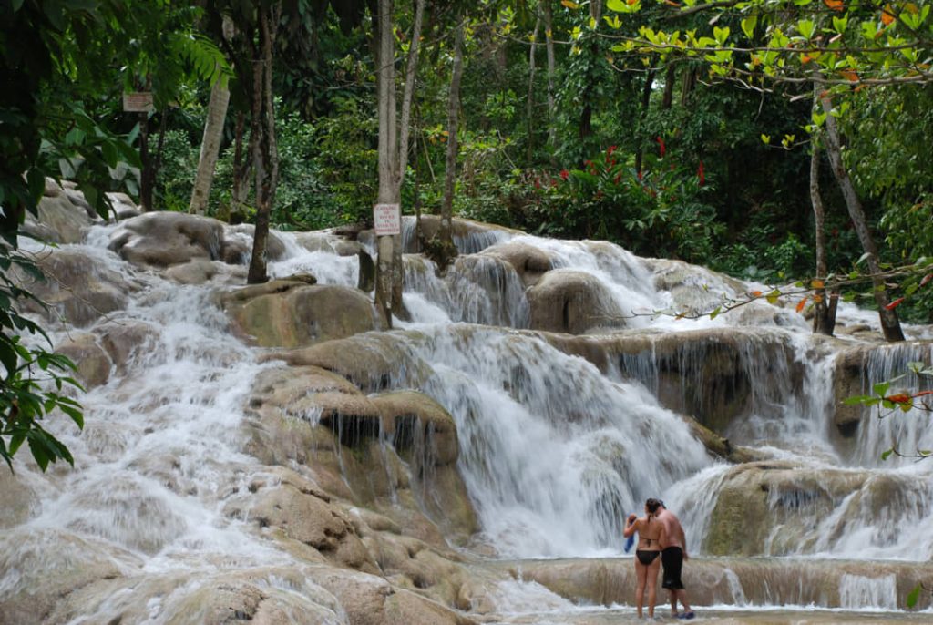 Een koppel staat onderaan de kalkstenen watervaltrappen van Dunn's River Falls tussen bomen in Jamaica