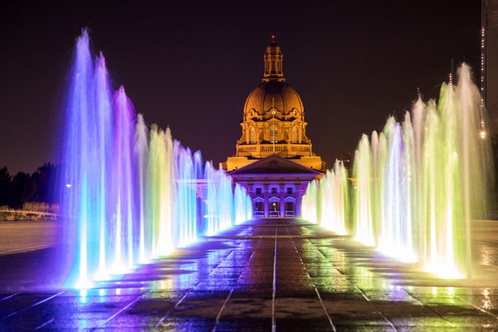 Kleurrijk verlichte fonteinen voor het regeringsgebouw Alberta Legislature in Edmonton bij nacht met de koepel op de achtergrond