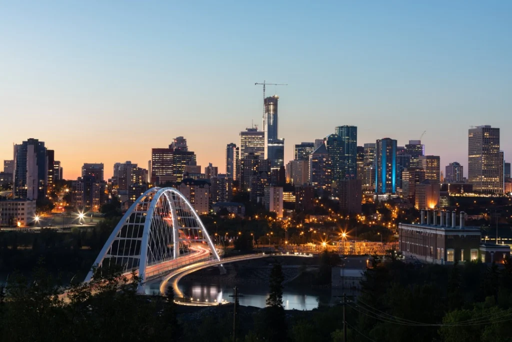 De verlichte skyline van Edmonton met een boogvormige brug over de rivier bij zonsondergang