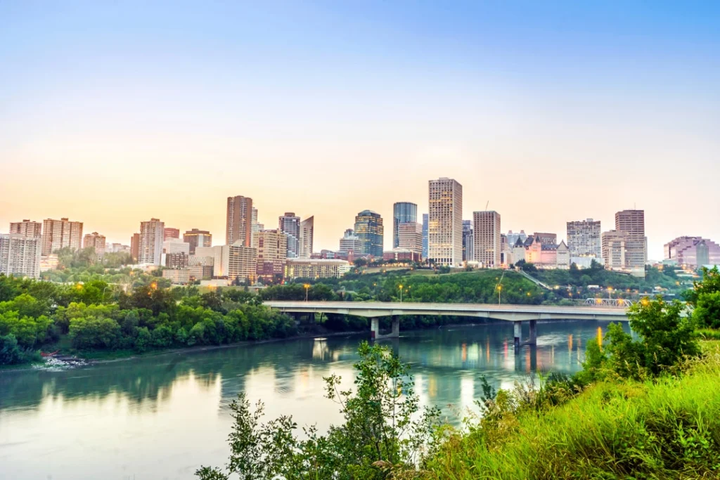 Uitzicht op de skyline van Edmonton met wolkenkrabbers, een brug over de rivier en groene oevers op de voorgrond