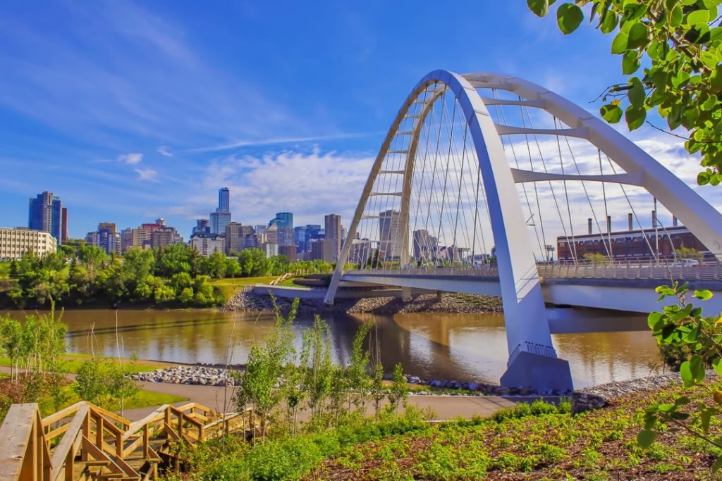 Witte boogbrug Walterdale Bridge over de rivier met de skyline van Edmonton op de achtergrond onder een blauwe lucht