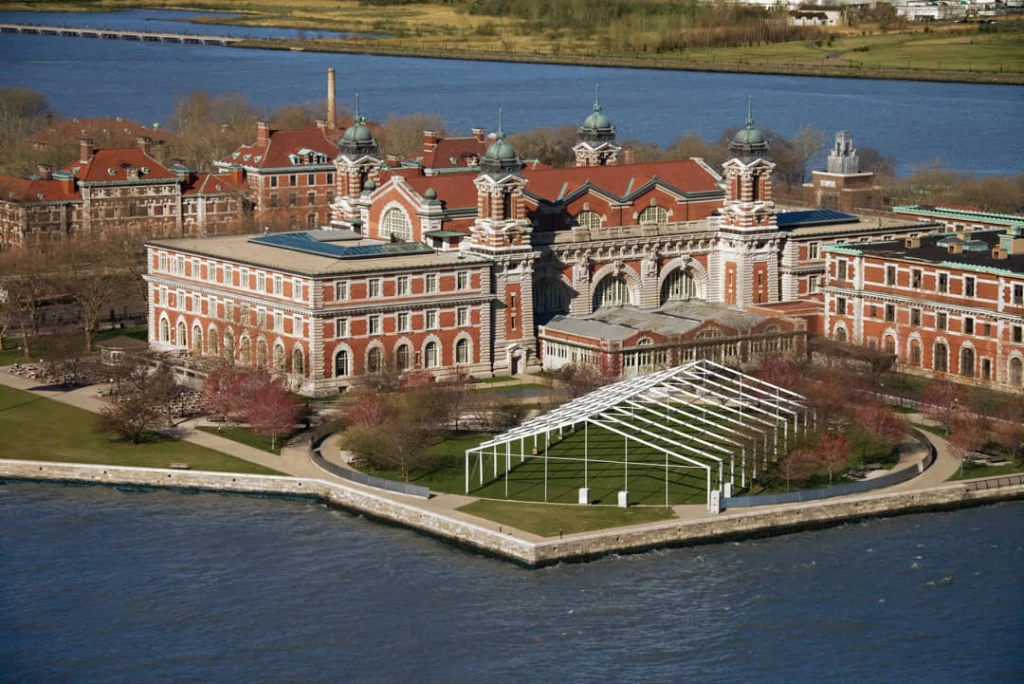 Glazen en stalen overkapping bij de ingang van het hoofdgebouw van Ellis Island met de klokkentoren en gevel erachter