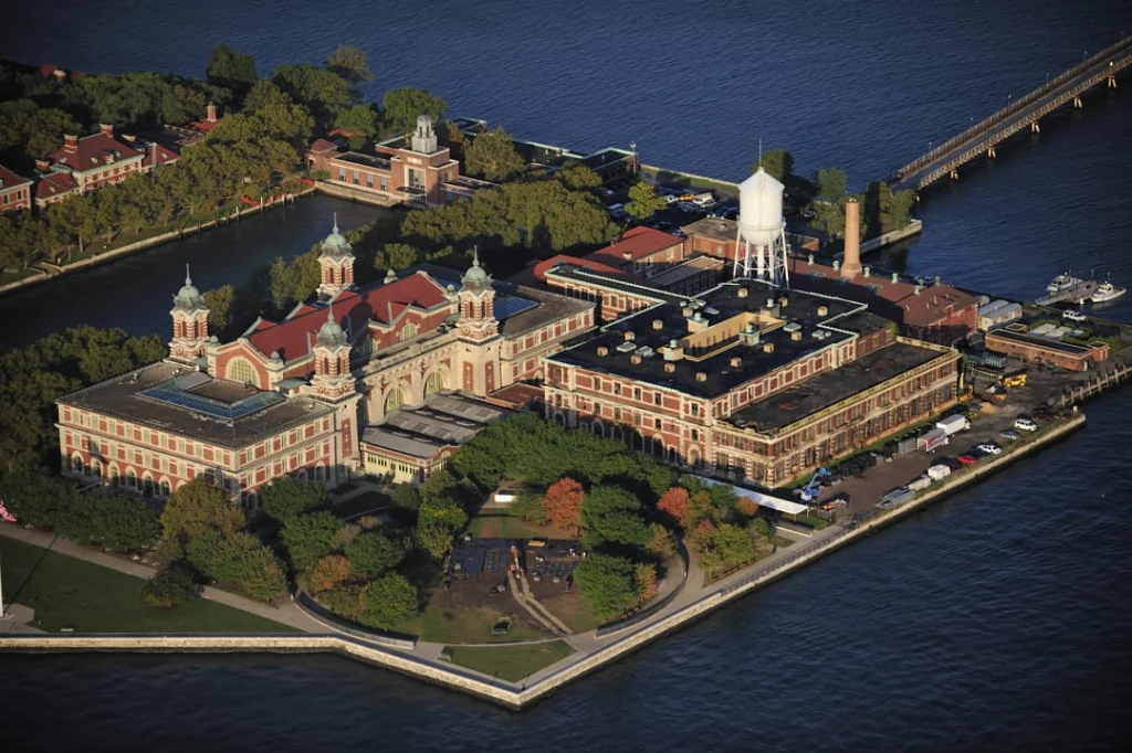 Luchtfoto van de rode dakenrij van Ellis Island met een witte watertoren, een schoorsteen en een lange steiger