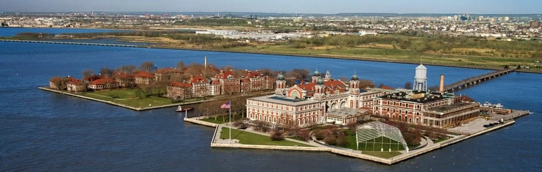 Luchtfoto van Ellis Island met zijn rode dakenrij en watertoren omringd door blauw water in de baai van New York