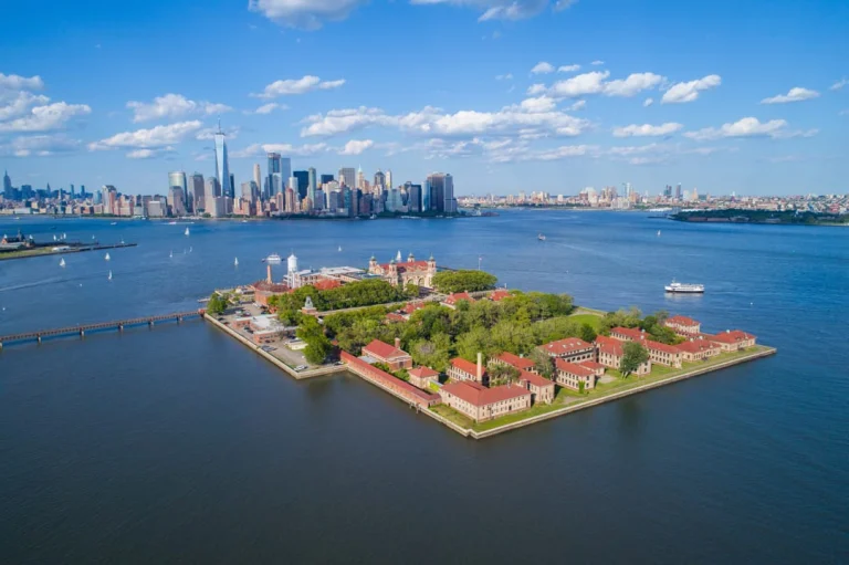 Luchtfoto van de rode gebouwen van Ellis Island omringd door water met de wolkenkrabbers van Manhattan zichtbaar aan de horizon