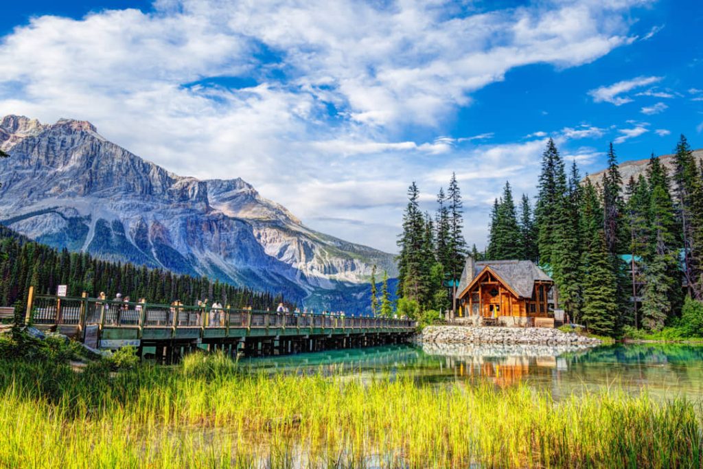 Turquoise water van Emerald Lake met een lange houten voetgangersbrug naar een houten lodge tussen dennenbomen en bergen