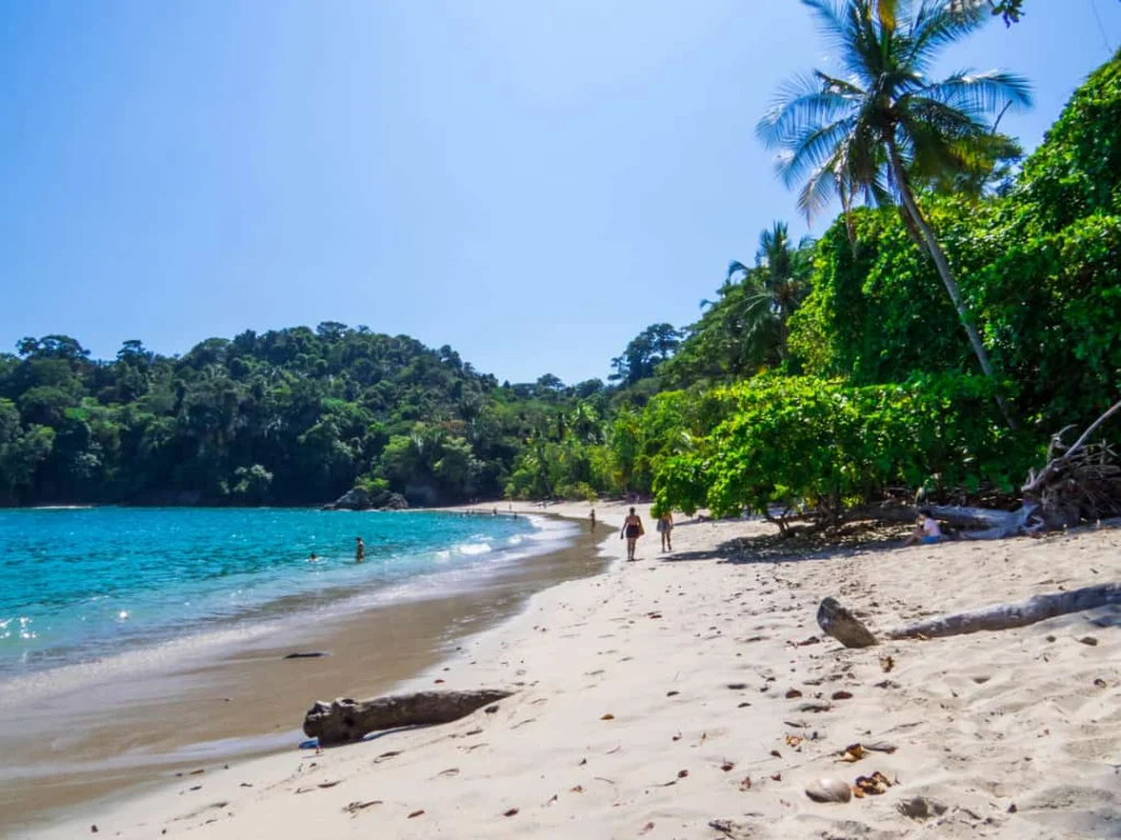 Twee wandelaars lopen over een verlaten strand met turkooizen zee en overhangende jungle op Escondido Beach in Costa Rica