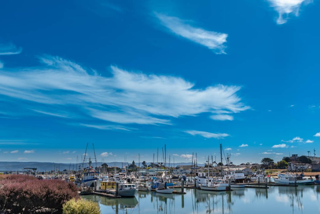 Rijen gemeerde zeilboten en vissersboten in een jachthaven met wolkenslierten aan een helderblauwe hemel bij Eureka