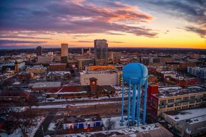 Luchtfoto van de skyline van Fargo met kantoorgebouwen en een grote blauwe watertoren onder een kleurrijke avondlucht