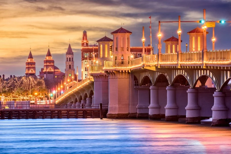 De verlichte Bridge of Lions en torenspitsen van St. Augustine in Florida weerspiegelen in het water tijdens een kleurrijke zonsondergang