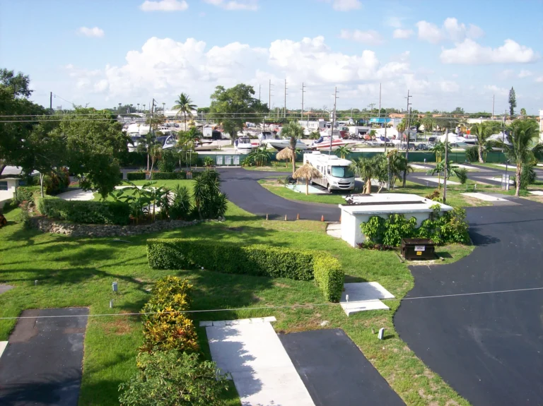 Luchtfoto van een RV-park in Fort Lauderdale met camperplekken, palmbomen, groene hagen en op de achtergrond een jachthaven met boten