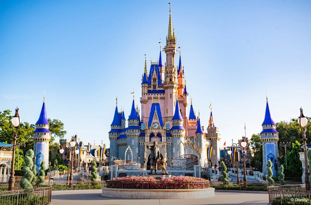 Het roze met blauwe torenspitsen van Cinderella Castle in Magic Kingdom onder een strakblauwe lucht met beelden op het plein