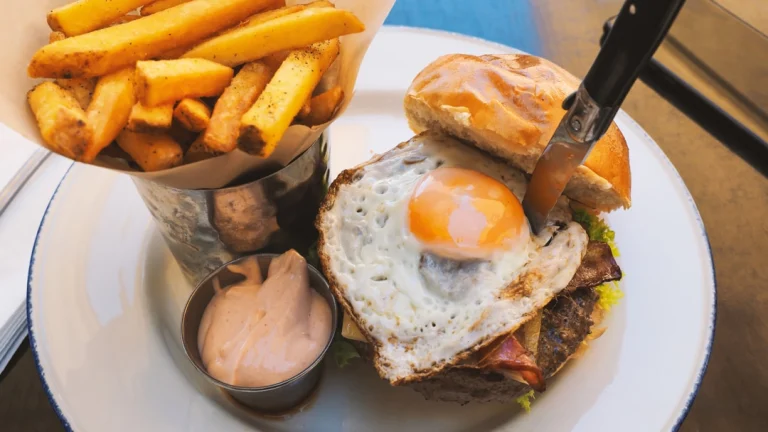 Bord met een hamburger belegd met een spiegelei en spek, geserveerd met friet en een dipsausje in Miami