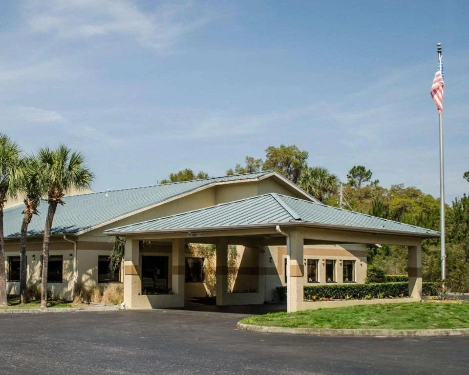 Ingang van een laag hotelgebouw in Crystal River, Florida, met een overdekte oprit, palmbomen en een Amerikaanse vlag