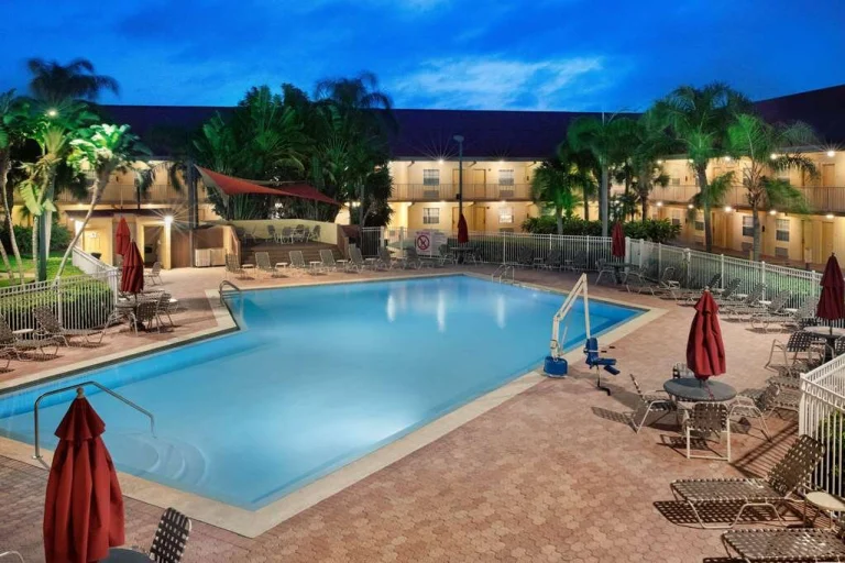 Een hotelzwembad met ligstoelen en parasols, verlicht in de avondschemering, omringd door palmbomen in Cocoa Beach, Florida