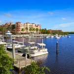 Een jachthaven in Napels, Florida, met witte boten afgemeerd langs een steiger en pastelkleurige appartementengebouwen op de achtergrond