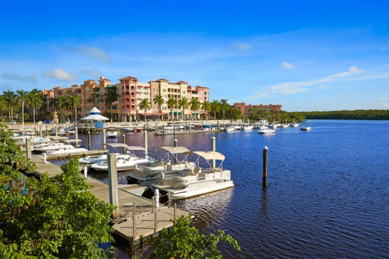Een jachthaven in Napels, Florida, met witte boten afgemeerd langs een steiger en pastelkleurige appartementengebouwen op de achtergrond