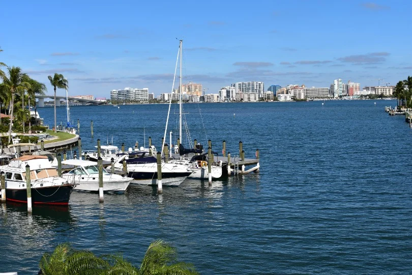 Meerdere jachten liggen afgemeerd in een jachthaven in Florida met de skyline van de stad op de achtergrond onder een blauwe hemel