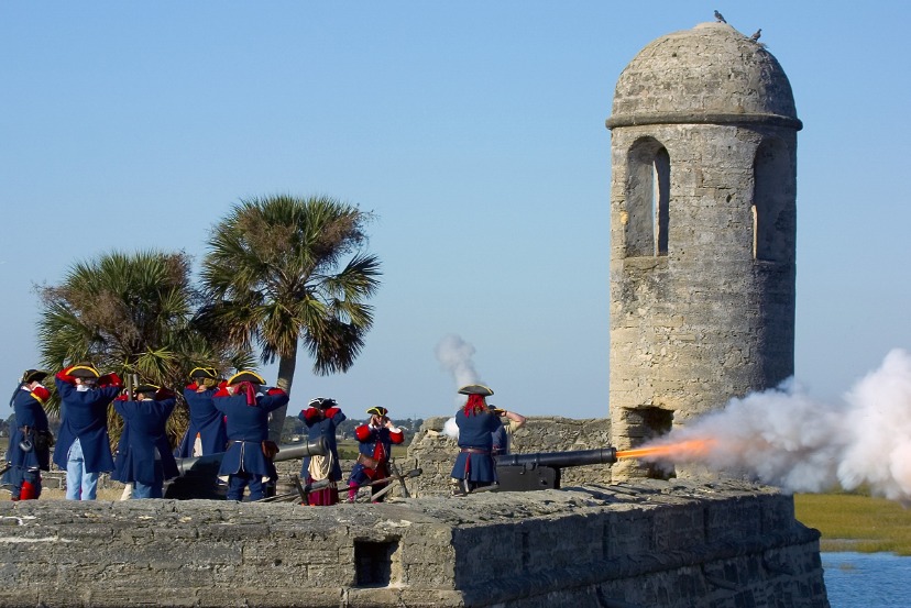 Geüniformeerde figuranten vuren een kanon af vanaf de muur van het stenen fort in Saint Augustine, Florida, met een wachttoren en palmbomen op de achtergrond