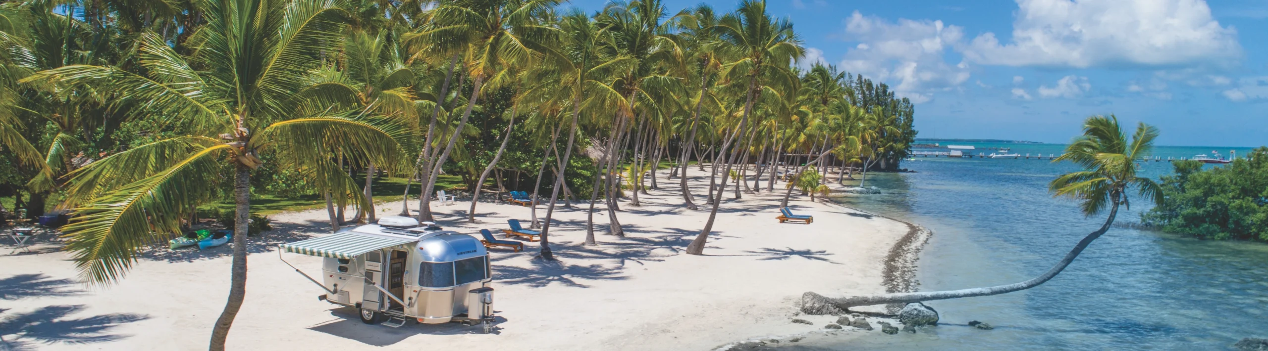 Een glimmende camper met luifel staat op een wit zandstrand tussen palmbomen aan zee in de Florida Keys