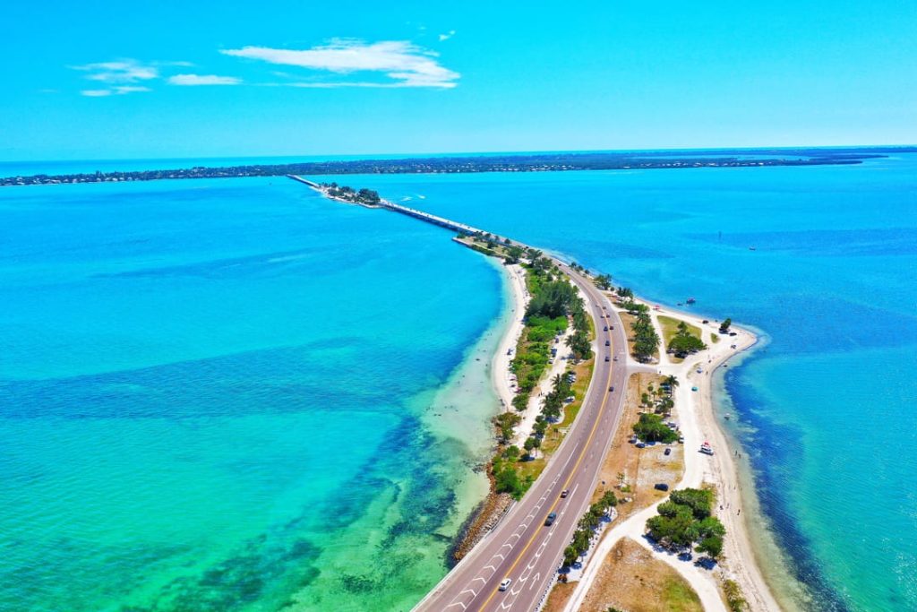 Luchtfoto van een lange weg over een brug tussen helder turquoise en dieper blauw zeewater