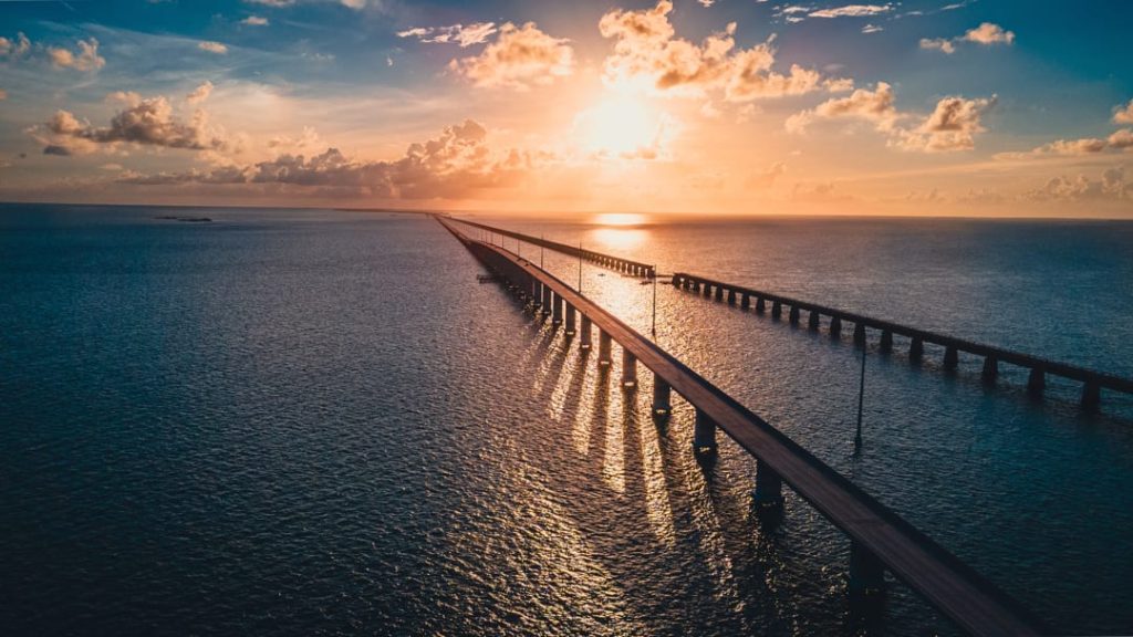 Lange brug over de zee weerspiegelt de ondergaande zon met een gouden gloed op het rustige water
