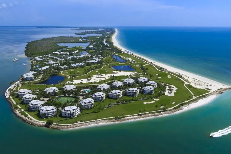 Luchtfoto van een smal eiland bij Fort Myers met een golfresort, appartementencomplexen, palmbomen en een wit zandstrand omgeven door helderblauw water