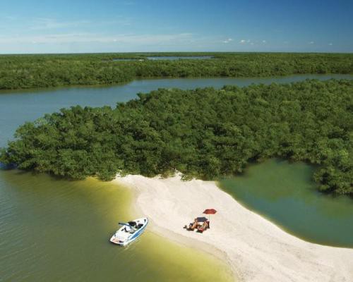 Luchtfoto van een afgelegen zandeiland omringd door mangroven met een aangemeerde boot en een parasol op het strand