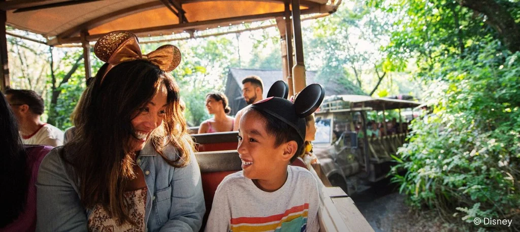 Moeder en zoon met Mickey oren lachen naar elkaar tijdens een tocht door groen begroeide paden in Magic Kingdom