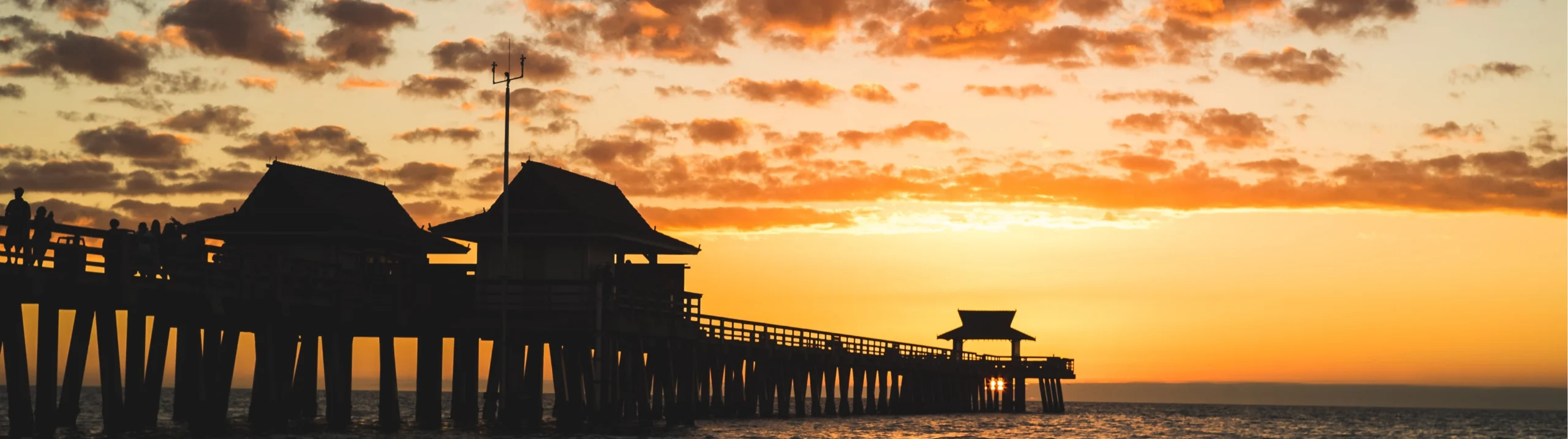 De houten pier van Naples in Florida steekt donker af tegen een oranje gekleurde luchte bij zonsondergang boven zee