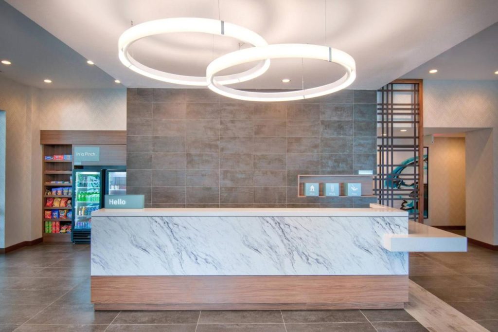 Marmeren receptiebalie in een hotellobby met ronde hanglampen, een muur van keramische tegels en een kleine snackshop op de achtergrond