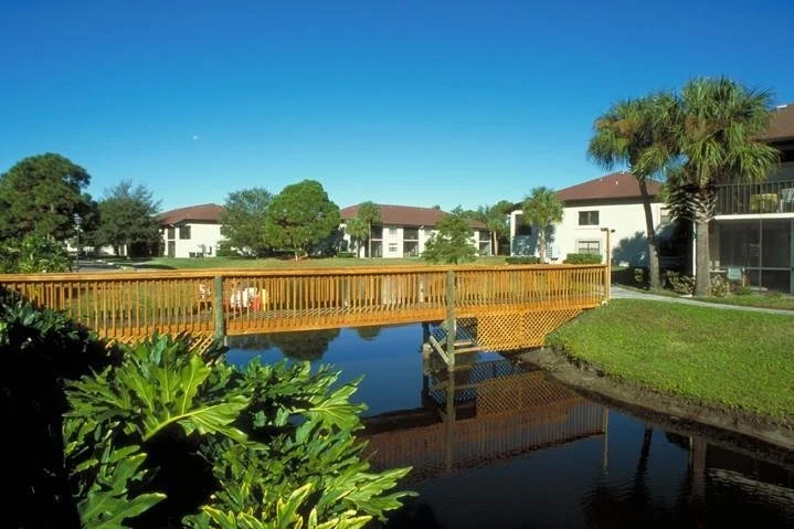 Een houten voetgangersbrug met palmbomen leidt over een kalme vijver naar vakantieappartementen in Sarasota, Florida