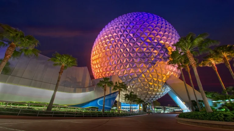 De bolvormige attractie Spaceship Earth van EPCOT kleurrijk verlicht tussen palmbomen tijdens de avondschemering