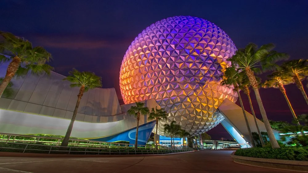 De bolvormige attractie Spaceship Earth van EPCOT kleurrijk verlicht tussen palmbomen tijdens de avondschemering