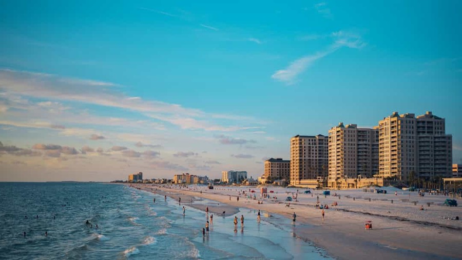 Breed zandstrand in Clearwater Beach, Florida, met wandelaars langs de zee en hoge hotels op de achtergrond