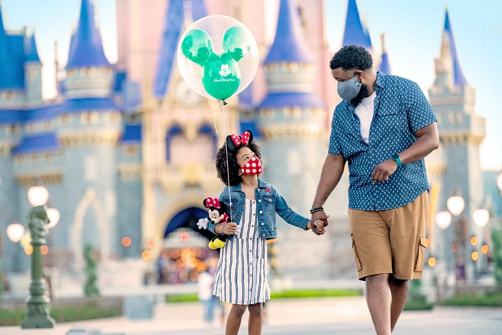 Vader en dochter met Mickey en Minnie oren wandelen hand in hand met een ballon voor het roze kasteel