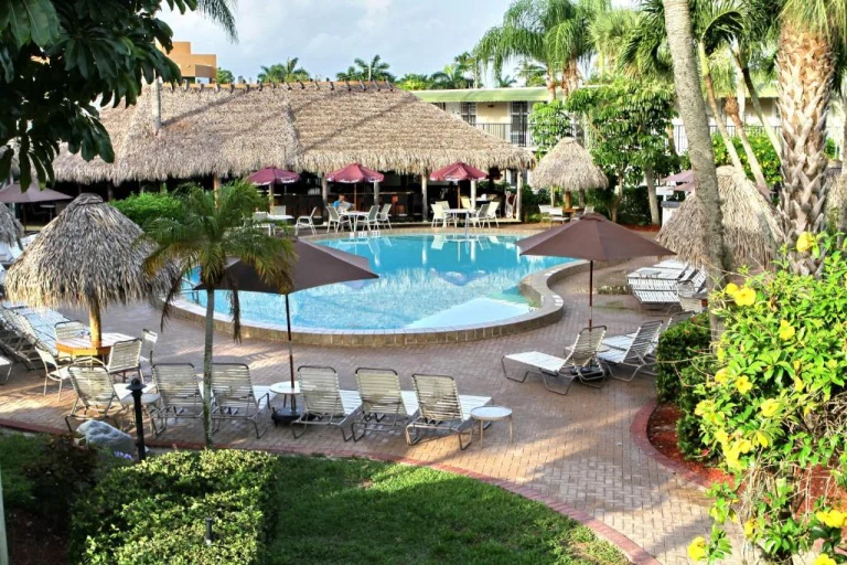 Zwembad omgeven door loungestoelen, parasols en rieten palapa's bij een hotel in Naples-Marco Island in Florida