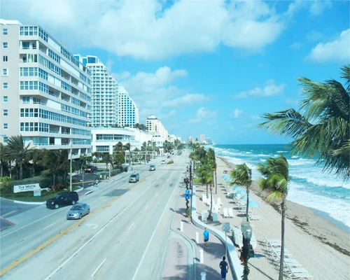 Brede boulevard met hardlopers en palmbomen tussen hotels en het strand met golvende zee in Fort Lauderdale