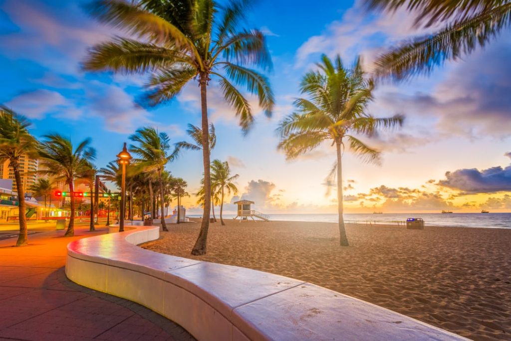 Gebogen strandpromenade met palmbomen langs het strand terwijl de zon opkomt boven zee in Fort Lauderdale