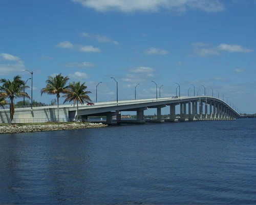 Lange betonnen boogbrug met lantaarnpalen en palmbomen aan de oever, over kalm blauw water bij Fort Myers