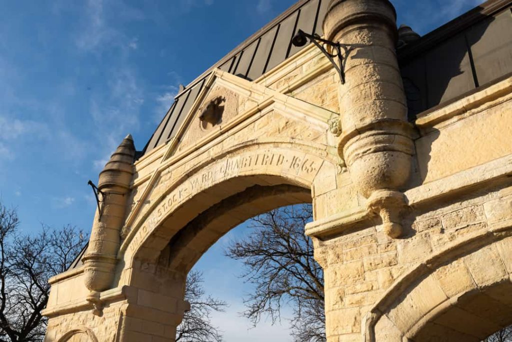 Gedetailleerd uitgehouwen stenen poort met de tekst stockyards quartered 1866, gezien van onderaf tegen een blauwe lucht