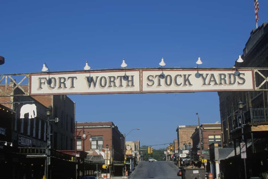 Groot wit straatbord met de tekst fort worth stock yards, opgehangen boven een winkelstraat met historische gebouwen