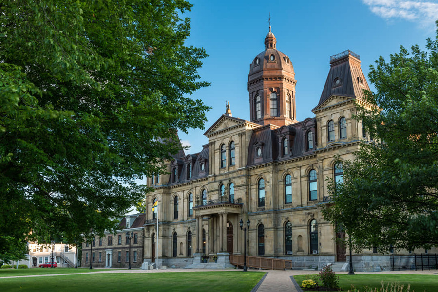 Een statig negentiende-eeuws gebouw met een rode koepeltoren en booggewelfde ramen staat achter een groen gazon in Fredericton, New Brunswick